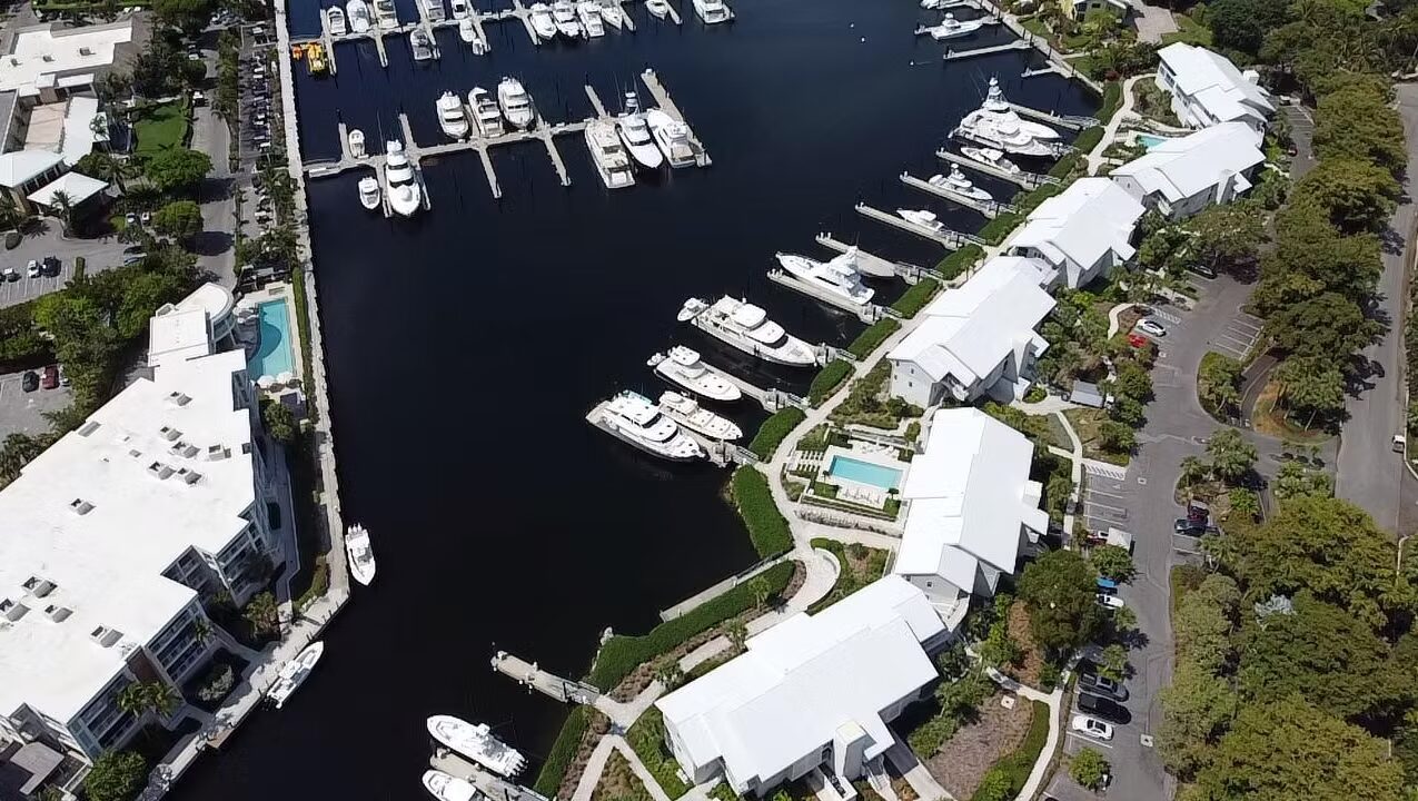 Aerial view of a marina with yachts docked alongside white buildings.