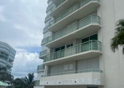 A multi-story white building with balconies against a cloudy sky, adjacent to an empty parking lot.