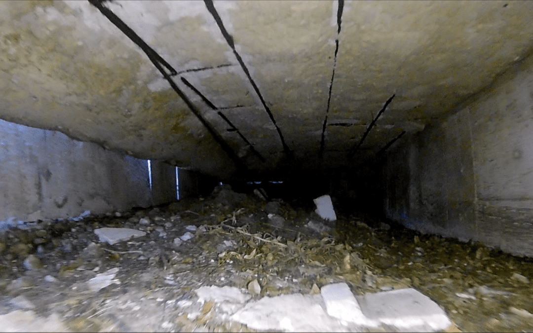 Narrow concrete underpass with debris and sparse light at the end.